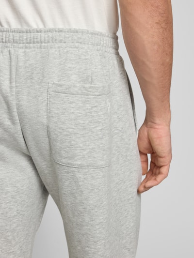 Männermodel trägt Sweathose mit Biese und Varsiety Embleme von Review, hellgrauer Baumwoll-Mix mit Stretch-Anteil, Gesäßtasche, Nahaufnahme Rückansicht.