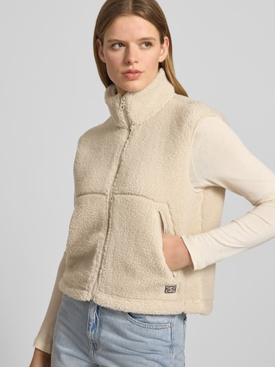 Vrouwenmodel draagt bodywarmer van teddybont met opstaande kraag, recht model, ritssluiting, zij-ritszakken, labelpatch, model 'MASEY' van Noisy May, ruglengte maat S 52 cm, schouderbreedte 44 cm, borstwijdte 52 cm, kleuren: crème, textuur: zacht. Halfclose-up voorkant.