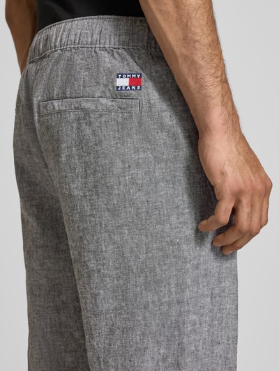 Männermodel trägt Regular Fit wijdte broek uit mix van linnen en katoen van Tommy Jeans, melangelook, labelstitching, detailopname rechterheup