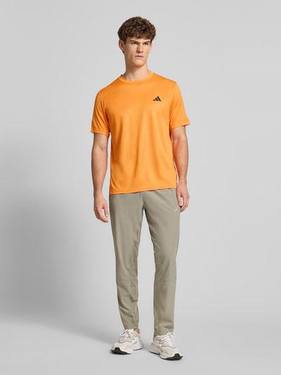 Männermodel trägt T-Shirt mit Logo und Rundhalsausschnitt von adidas Training in Orange, Regular Fit, Ganzkörperansicht von vorne.