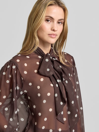 Vrouwenmodel draagt Relaxed Fit Bluse in semi-transparant design van SWING, bruine blouse met witte stippen, sierstrik, met lange mouwen, ruglengte bij maat 36 68 cm, nahaufnahme bovenlichaam.