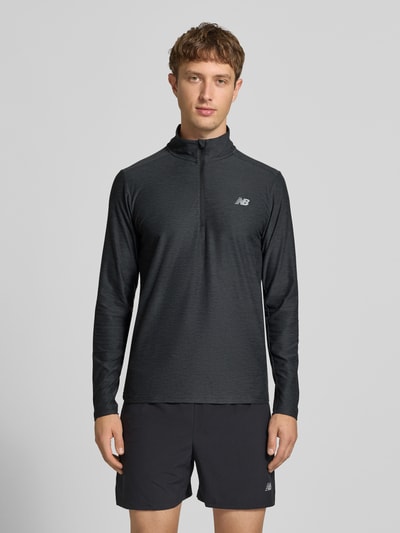 Männermodel trägt Regular Fit Sweatshirt mit Troyer-Kragen von New Balance, schwarz, Logo-Print, elastisch, Langarm, Ganzkörperansicht von vorne.