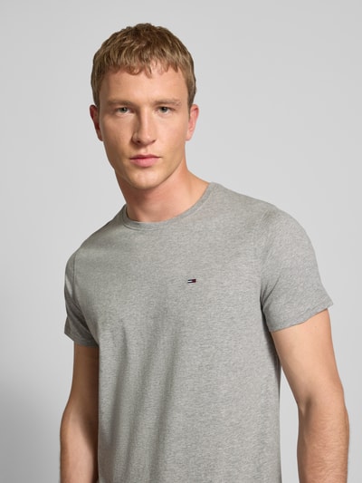 Męski model nosi T-shirt in Melange-Optik od Tommy Jeans z bawełny, prosty krój, efekt melanżu, okrągły dekolt, wyhaftowane logo, z przodu półzbliżenie.