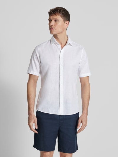 Męski model nosi Slim Fit Freizeithemd aus Leinen-Mix von Jake*s, mieszanka bawełny i lnu, krótki rękaw, kołnierzyk typu kent, krój slim fit, listwa guzikowa, długość tyłu w rozmiarze M 73 cm, szerokość ramion w rozmiarze M 47 cm, długość rękawa w rozmiarze M 26 cm, kolor biały, gładka struktura, Ganzkörperansicht z przodu.