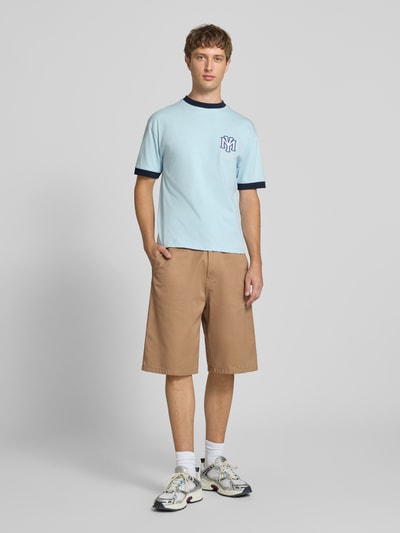 Männermodel trägt Bermudas mit Baumwoll-Anteil Modell 'Brader' von Carhartt Work In Progress in Beige, Relaxed Fit, Ganzkörperansicht von vorne. Material-Mix, Bundweite 44 cm, Innenbeinlänge 30 cm, Eingriff- und Gesäßtaschen, Gürtelschlaufen, Knopf- und Reißverschluss.