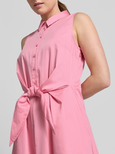 Frauenmodel trägt Hemdblusenkleid aus Satin in Midilänge von Comma in Rosa, taillierte Passform, Hemdblusenkragen, Ärmelloses-Design, durchgängige Knopfleiste, abnehmbares Taillenband, Material aus elastischem Baumwoll-Mix, weiche Satin-Optik, Ganzkörperansicht von vorne.