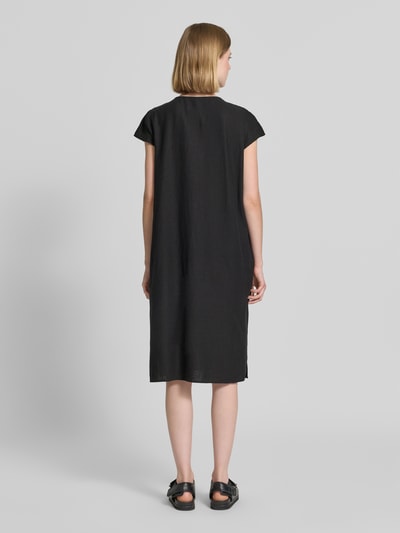 Frauenmodel trägt knielanges Leinenkleid mit V-Ausschnitt Modell 'Ina' von Soyaconcept in Schwarz, lockere Passform, Rückansicht Ganzkörperansicht. Locker fallendes Material mit Leinen-Mix und Viskose, seitliche Schlitze, kurze Ärmel.