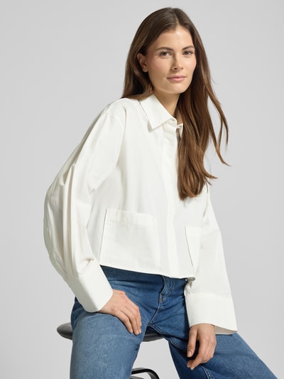 Modelka nosi Bluzka koszulowa Relaxed Fit Hemdbluse mit aufgesetzter Tasche Model 'Lee' od YAS z bawełny, białe odcienie, kieszeń, długie rękawy, kołnierzyk koszulowy, listwa guzikowa; długość tyłu 50 cm, długość rękawów 56 cm, widok całej sylwetki z przodu.
