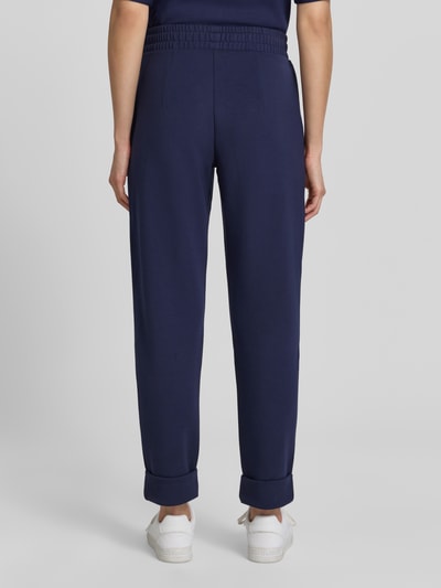 Frauenmodel trägt Straight Fit Sweatpants in verkürzter Passform von Christian Berg Woman in Dunkelblau, Elastischer-Material-Mix, Bundfalten, Ganzkörperansicht Rückansicht.