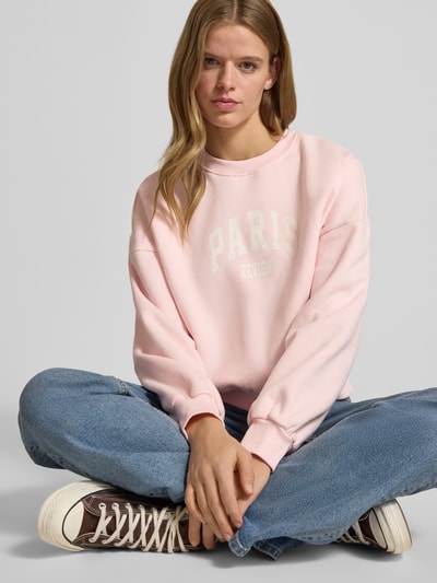Frauenmodel trägt Sweatshirt mit Label-Print und Rundhalsausschnitt von Review, rosa Farbe, Baumwoll-Mix, Relaxed-Fit, Ganzkörperansicht von vorne.