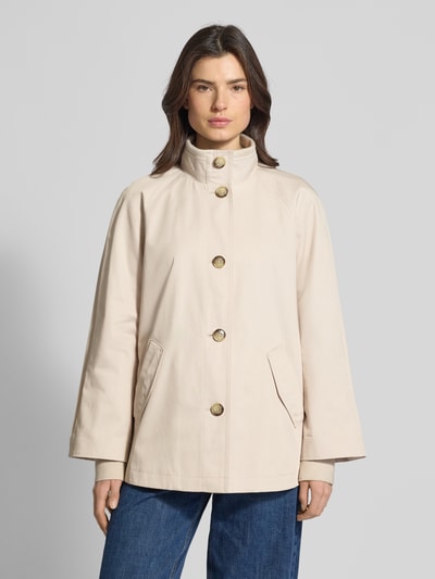 Modelka nosi Relaxed Fit Jacke mit Stehkragen od comma, mieszanka bawełny, wpuszczane kieszenie, stójka, listwa guzikowa, krój relaxed fit, jasny beż, gładka tekstura, długość tyłu w rozmiarze S: 70 cm, szerokość ramion w rozmiarze S: 48 cm, szerokość klatki piersiowej w rozmiarze S: 58 cm, długość rękawów w rozmiarze S: 73 cm. Ganzkörperansicht z przodu.