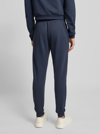 Mężczyzna nosi Spodnie dresowe z elastycznym pasem i nadrukiem z logo od EA7 Emporio Armani, bawełna, krój regular fit, długość wewnętrzna 78 cm, widok całej sylwetki od tyłu.