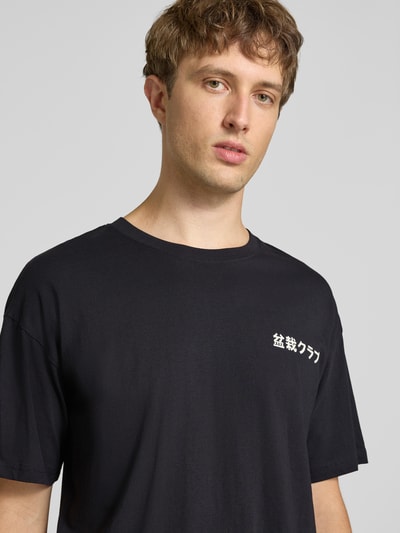 Männermodel trägt Relaxed Fit T-Shirt aus reiner Baumwolle Modell "DYLAN" von JACK & JONES, Print-Detail, schwarze Farbe, Nahaufnahme Oberkörper.