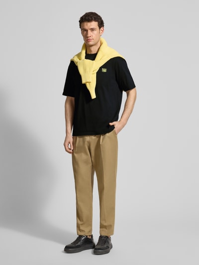 Männermodel trägt Regular Fit T-Shirt aus reiner Baumwolle Modell 'TE-BRUTALISM' von BOSS Orange in Schwarz, Label-Applikation, Ganzkörperansicht von vorne.