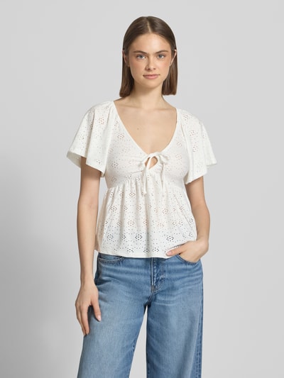 Modelka kobieca nosi Slim Fit T-Shirt mit tiefem V-Ausschnitt Modell 'SMILLA' von Only w białym, półprzezroczystym, kwiatowym wzorze, krój slim fit, krótki rękaw, materiał stretch, widok całej sylwetki z przodu.
