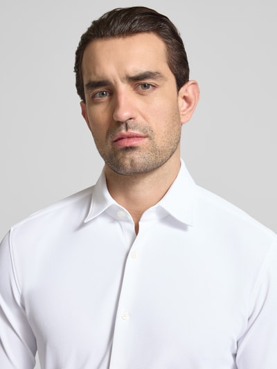 Männermodel trägt weißes Slim Fit Businesshemd in Struktur-Optik Modell 'ERMO' von HUGO aus Piqué, Kentkragen, durchgehende Knopfleiste, Logo-Stitching, Nahaufnahme Oberkörper.