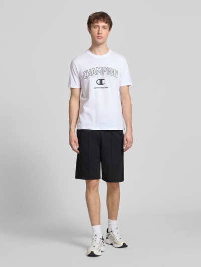 Männermodel trägt Bermudas mit elastischem Bund und Label-Stitching von CHAMPION, Regular Fit, Baumwoll-Mix, schwarze Farbe, Ganzkörperansicht von vorne.