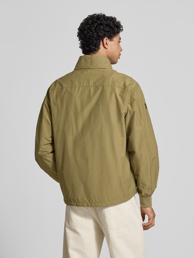 Mężczyznamodel nosi kurtkę z stójką model 'Flyweight' od Superdry, krój regular fit, zamek błyskawiczny, oliwkowy kolor, długość tyłu w rozmiarze M: 71 cm, szerokość ramion w rozmiarze M: 45 cm, szerokość klatki piersiowej w rozmiarze M: 53 cm, długość rękawów w rozmiarze M: 66 cm, całkowity widok od tyłu.