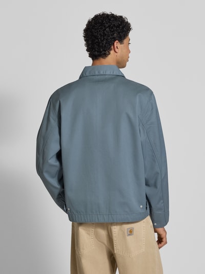 Männermodel trägt Jacke mit Label-Stitching und Eingrifftaschen von Carhartt Work In Progress in Blau, Ganzkörperansicht Rückansicht. Regular Fit, Umlegekragen, Reißverschluss, Rückenlänge 68 cm, Schulterbreite 59 cm, Brustweite 60 cm, Ärmellänge 20 cm.