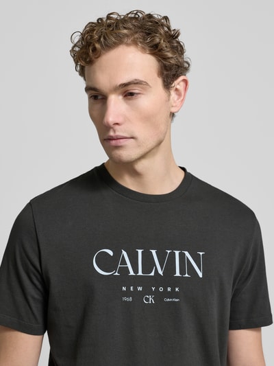 Männermodel trägt T-Shirt mit Label-Print und Rundhalsausschnitt von CK Calvin Klein in Schwarz, reine Baumwolle, Regular-Fit, Nahaufnahme Oberkörper.
