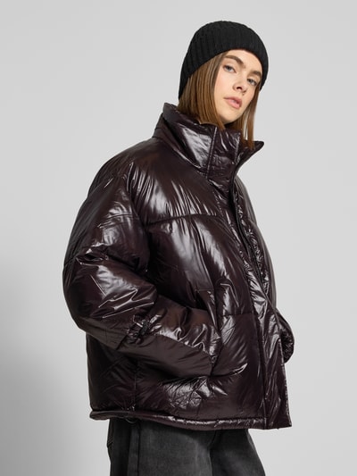 Modelka nosi błyszczącą, ciemnofioletową steppjackę z wysokim kołnierzem Steppjacke mit Stehkragen Modell 'ALLIE' od Noisy May, długość do bioder, widok z przodu, zdjęcie w kontekście: wygodny fason relaxed fit, zakryty zamek, kieszenie boczne, wymiary rozmiaru S.