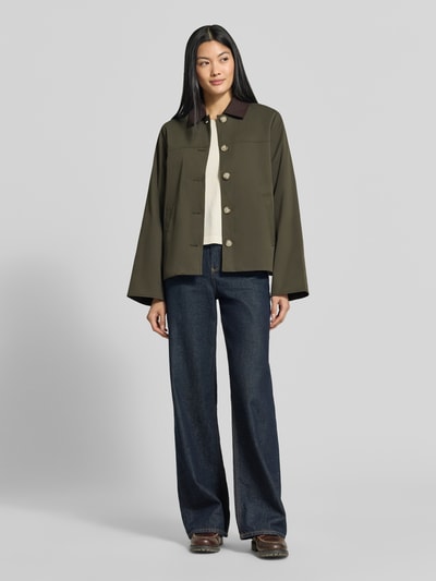 Kobiece model nosi Regular Fit Blouson mit Umlegekragen Modell 'CHELSEAPOPPY' od VERO MODA, oliwkowa z beżowymi guzikami, szerokie rękawy, prosta faktura, dżinsy ciemnoniebieskie, bomberka damska, całopostaciowy widok z przodu.