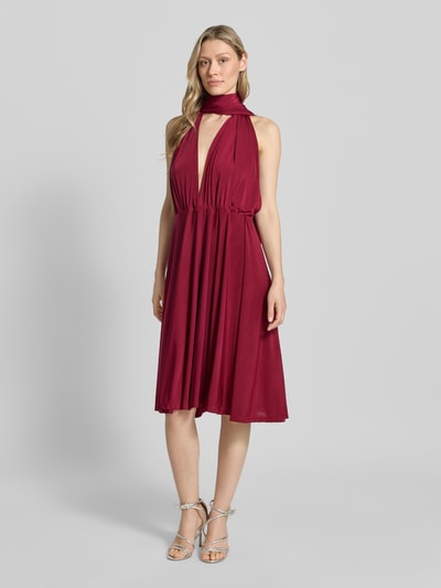 Vrouwenmodel draagt 'Knielanges Cocktailkleid mit tiefem V-Ausschnitt' van Rose Avenue in bordeauxrood, getailleerde fit, knielengte, diepe V-hals, gekruiste bandjes achter, tailleband, ruglengte maat S 44 cm, full-body vooraanzicht.