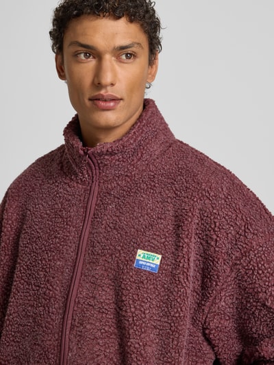 Männermodel trägt Fleecejacke mit Stehkragen Modell 'HOKTOWN' von American Vintage, Label-Detail, Relaxed-Fit, Nahaufnahme Oberkörper.