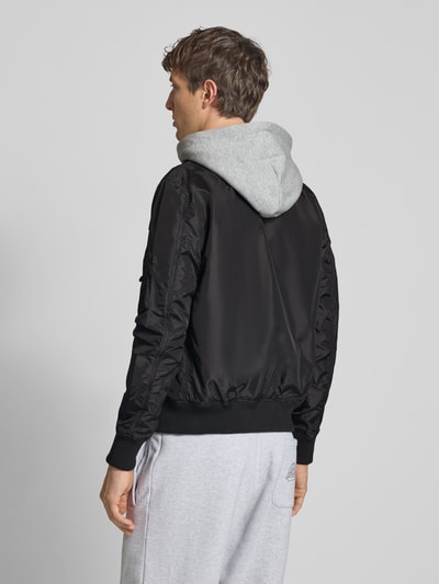 Männermodel trägt Blouson mit Logo-Anhänger Modell 'MA-1 TT' von Alpha Industries mit Kapuze aus Sweat, Rückansicht Ganzkörperansicht.