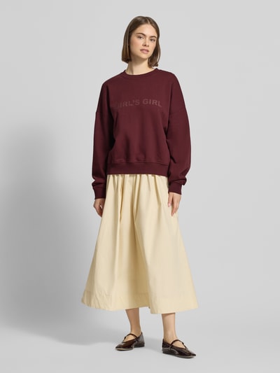 Frauenmodel trägt Sweatshirt mit Statement-Print und überschnittenen Schultern von OH APRIL aus Reine Baumwolle, Regular-Fit, Gerippter Rundhalsausschnitt, Gerippte-Abschlüsse, bordeaux und beige Farbkombination, glatte Textur, Ganzkörperansicht von vorne.