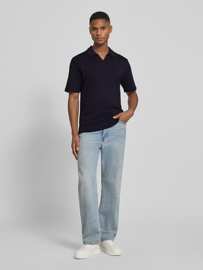 Männermodel trägt Strickshirt mit V-Ausschnitt Modell 'MILANO' von Jack & Jones Premium, dunkelblau, Baumwoll-Mix, Gerader-Schnitt, Umlegekragen, Label-Detail, kombiniert mit hellblauer Jeans und weißen Schuhen, Rückenlänge bei Größe M: 69 cm, Ganzkörperansicht von vorne.