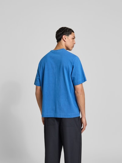 Männermodel trägt Relaxed Fit T-Shirt mit Logo-Stitching von Forét aus reiner Baumwolle, Kurzärmelig, in Blau und Schwarz, Ganzkörperansicht Rückansicht.
