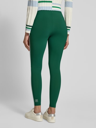 Männermodel trägt Slim Fit Leggins mit elastischem Bund von Marc Cain, elastyczna mieszanka materiałów, krój slim fit, ozdobne obszycie, szerokość w rozmiarze 36: 34 cm, długość wewnętrzna nogawki w rozmiarze 36: 76 cm, zielony kolor, gładka tekstura, całkowity widok od tyłu