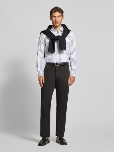 Männermodel trägt Straight Fit Chino aus Baumwoll-Mix Modell 'Miles' von Selected in Dunkelbraun, kombiniert mit hellem Hemd, Ganzkörperansicht von vorne. Herren Chino von Selected.