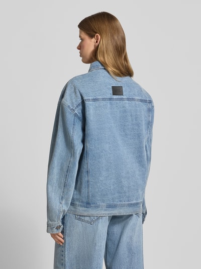 Frauenmodel trägt Jeansjacke mit rückseitigem Label-Patch von Karo Kauer aus Reine Baumwolle im Loose-Fit, hellblau, Ganzkörperansicht Rückansicht. Pattentaschen mit Knopfverschluss, seitliche Eingrifftaschen, Kentkragen, Knopfleiste, Rückenlänge bei Größe S 68 cm, Schulterbreite 60 cm, Brustweite 58 cm, Ärmellänge 60 cm.
