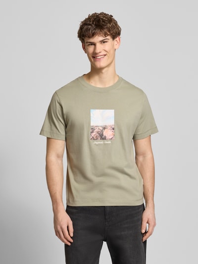 Männermodel trägt T-Shirt mit Rundhalsausschnitt Modell 'JORNORREBRO' von Jack & Jones aus reiner Baumwolle in hellem Khaki mit Frontprint, gerader Schnitt, Ganzkörperansicht von vorne.