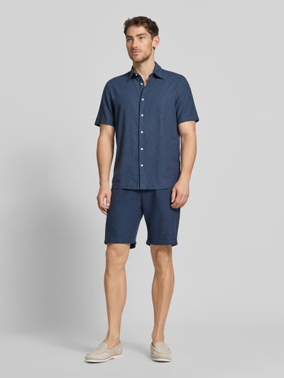 Męski model nosi Shorts aus Leinen-Baumwoll-Mix mit elastischem Bund od MCNEAL, ciemnoniebieski, krój regular fit, Szerokość w rozmiarze M 44 cm, długość nogawki 23 cm, Ganzkörperansicht von vorne.
