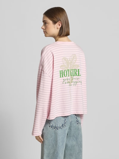 Frauenmodel trägt Longsleeve mit rückseitigem Statement-Print von OH APRIL in Rosa mit feinen Streifen, Reine Baumwolle, Loose-Fit, Rundhalsausschnitt, Überschnittene Schultern, Rückenlänge bei Größe S 53 cm, Ganzkörperansicht Rückansicht.