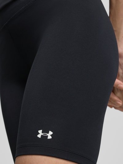 Frauenmodel trägt Radlerhose mit Logo von Under Armour in Schwarz, Material-Mix mit Stretch-Anteil, körpernahe Passform, Nahaufnahme Oberschenkel.