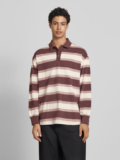 Männermodel trägt Regular Fit Poloshirt mit elastischen Ärmelabschlüssen von PUMA PERFORMANCE, braune und cremeweiße Streifen, Ganzkörperansicht von vorne. Reine Baumwolle, Langärmelig, Polokragen, Rückenlänge 75 cm, Ärmellänge 59 cm bei Größe M.