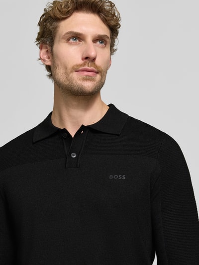 Männermodel trägt schwarzes Relaxed Fit Poloshirt mit Woll-Anteil Modell 'KN_Momentum-X PL' von BOSS, feine Textur, Nahaufnahme Oberkörper, Herren Poloshirt von BOSS Green.