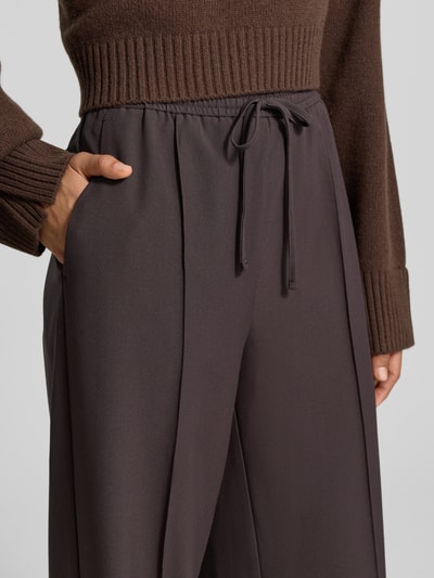 Frauenmodel trägt Wide Fit Sweatpants mit Viskose-Anteil von MYON, dunkelbraun, Zierfalten, elastischer Bund mit Tunnelzug, Nahaufnahme Oberkörper.