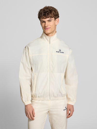 Męski model nosi Regular Fit kurtka ze stójką model 'Nayla' od SERGIO TACCHINI, kremowa, zamek błyskawiczny, wpuszczane kieszenie, elastyczne wykończenia, długość tyłu w rozmiarze M: 69 cm, długość rękawów w rozmiarze M: 61 cm, ujęcie: całkowity przód.