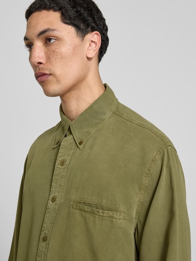 Männermodel trägt Freizeithemd aus reinem Lyocell von Filippa K in Olivgrün mit Brusttasche, Button-Down-Kragen, Relaxed-Fit, Nahaufnahme Oberkörper.