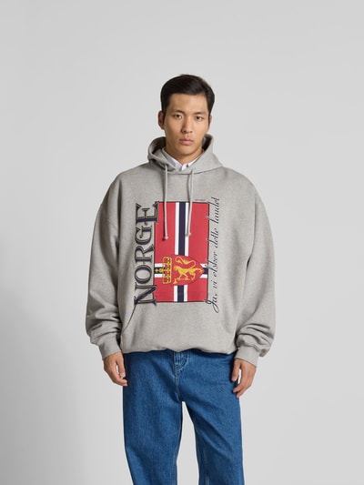 Männermodel trägt Oversized Hoodie mit Motiv-Print von VETEMENTS, Grau mit rotem und gelbem Print, Baumwoll-Mix, Ganzkörperansicht von vorne.