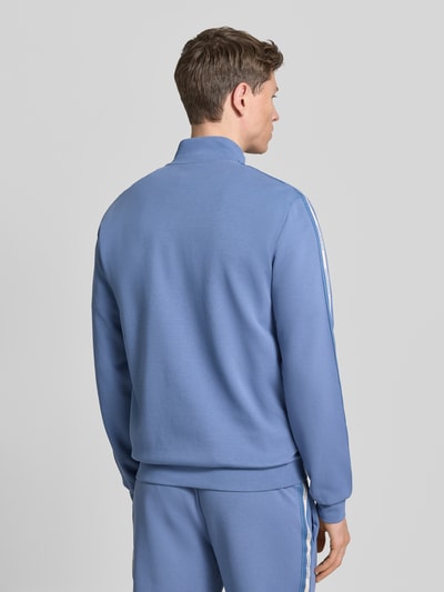Männermodel trägt Sweatjacke aus Baumwoll-Mix von EA7 Emporio Armani in Blau mit Galonstreifen, elastischen Abschlüssen, Rückenansicht.