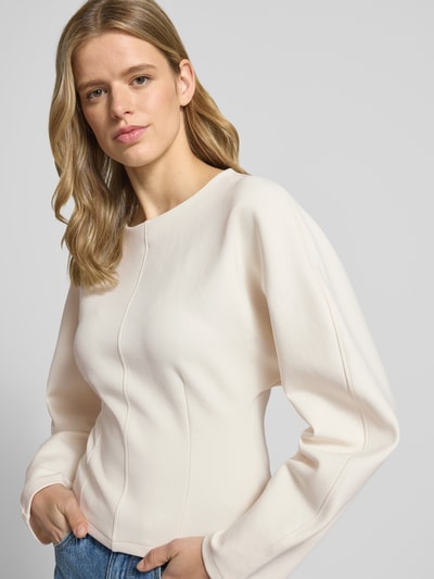 Modelka nosi Sweatshirt mit Rundhalsausschnitt od Gina Tricot, bawełniany miks ze stretchem, krój sculpted fit, lekko zaokrąglony dół, kolor kremowy, widok na górną część ciała z przodu.