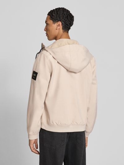 Männermodel trägt Regular Fit Jacke mit Logo-Detail von JACK & JONES in Beige, Kapuze, Softshell, elastische Abschlüsse, Ganzkörperansicht Rückansicht