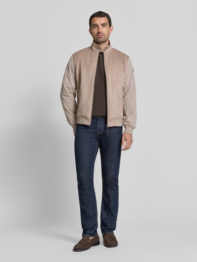 Męski model nosi kurtkę Jacke mit Stehkragen und Reißverschlusstaschen Modell 'Clunie' von JOOP!, beżowy kolor, krój regular fit, stójka, zamek błyskawiczny, kieszenie zapinane na zamek błyskawiczny, długość tyłu w rozmiarze 50: 67 cm, szerokość ramion w rozmiarze 50: 49 cm, szerokość klatki piersiowej w rozmiarze 50: 61 cm, długość rękawów w rozmiarze 50: 67 cm, pełny widok od przodu.