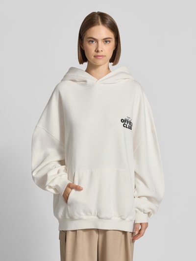 Frauenmodel trägt Oversized Hoodie mit Känguru-Tasche von Karo Kauer in Creme mit Label-Print und überschnittenen Schultern, Ganzkörperansicht von vorne.